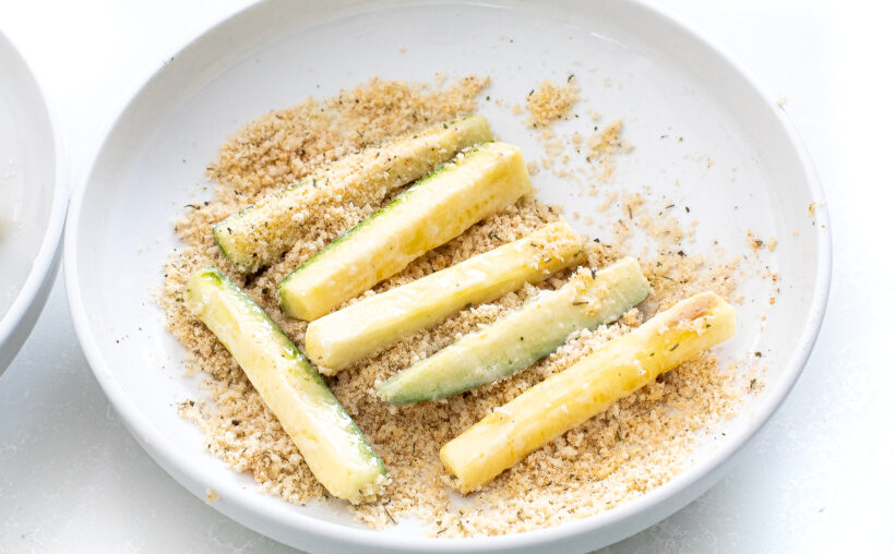 Zucchini spears being dipped into breading mixture.