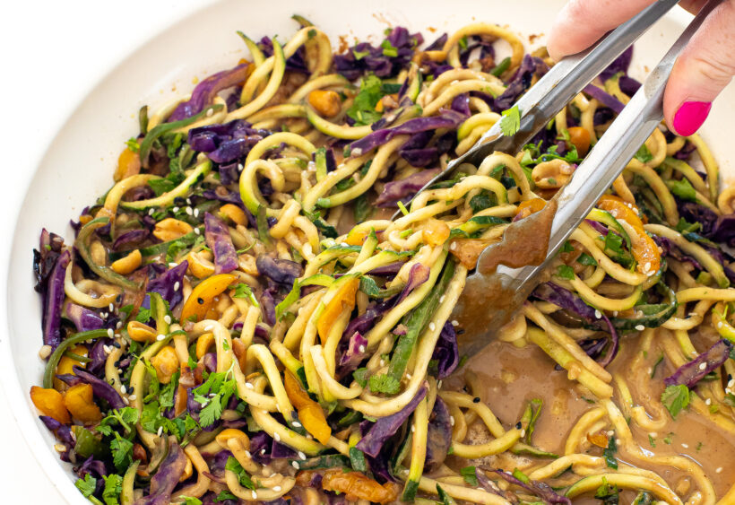 Zucchini noodles and vegetables being tossed with peanut sauce. 