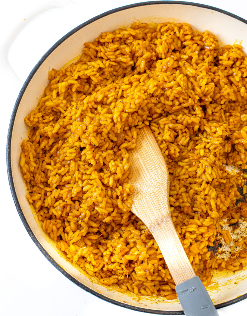 Close up view of turmeric rice in a large skillet with a wood spatula.