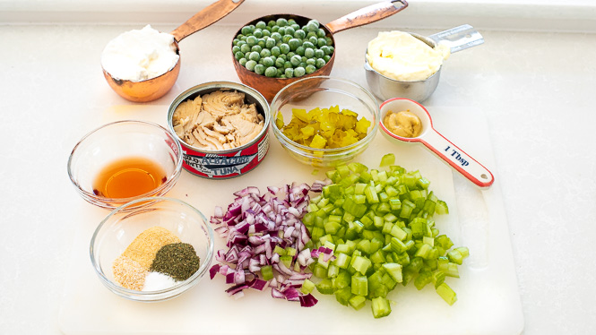 Ingredients needed for tuna macaroni salad on a white cutting board. 