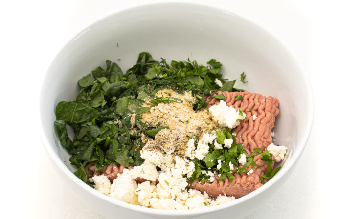 Ground turkey with additional ingredients in a white mixing bowl. 