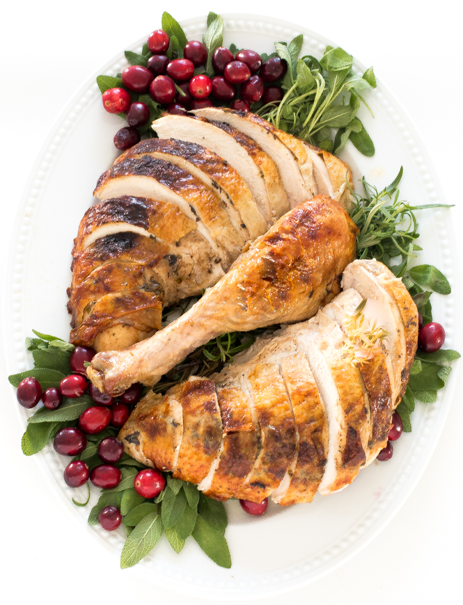 sliced roasted turkey on a serving tray with cranberries and herbs for garnish