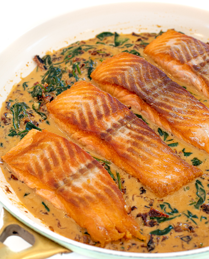 Salmon with a spinach tuscan sauce in a white pan.