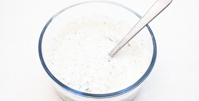 Sauce being mixed in a clear mixing bowl with a spoon.