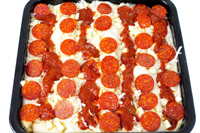 Pizza topped with cheese, pepperoni and lines of sauce.