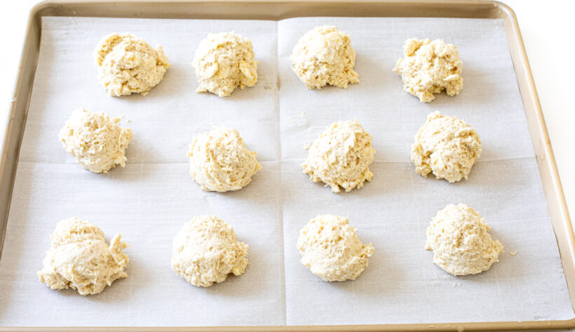 Biscuit dough dropped onto a baking sheet lined with parchment paper. 