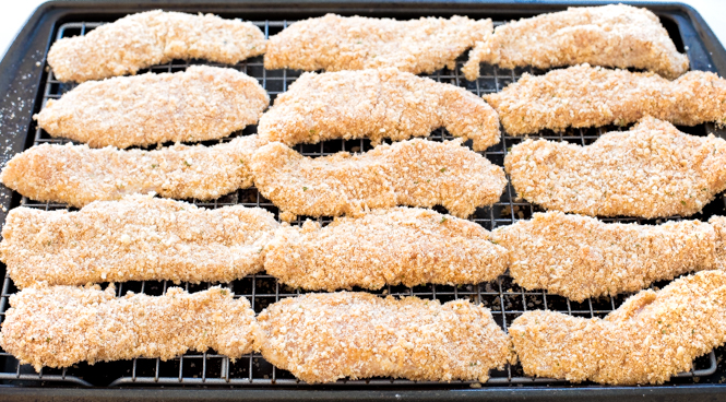 Unbaked breaded chicken tenderloins on a baking sheet lined with wire rack