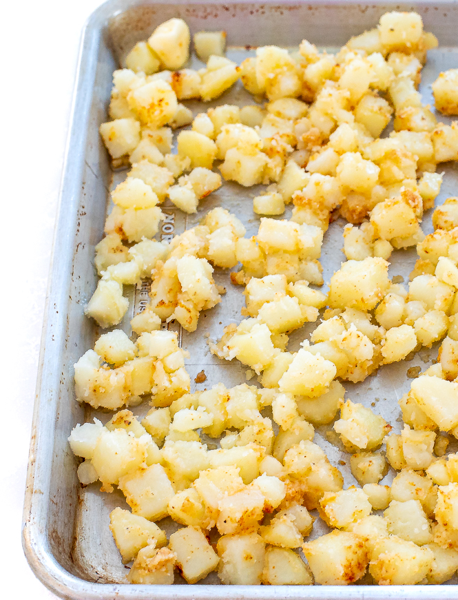 Diced potatoes spread out on a silver baking sheet.