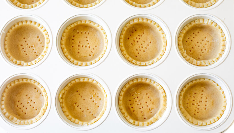 Unbaked tart dough in a muffin tin.
