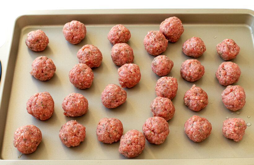 unbaked meatballs on a gold baking sheet