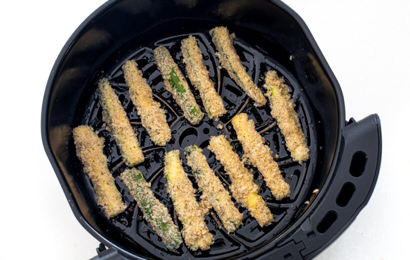 Zucchini fries in an air fryer basket before being cooked.
