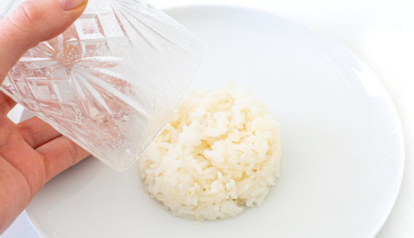 Hand holding a cup over a disk of sushi rice on a plate.