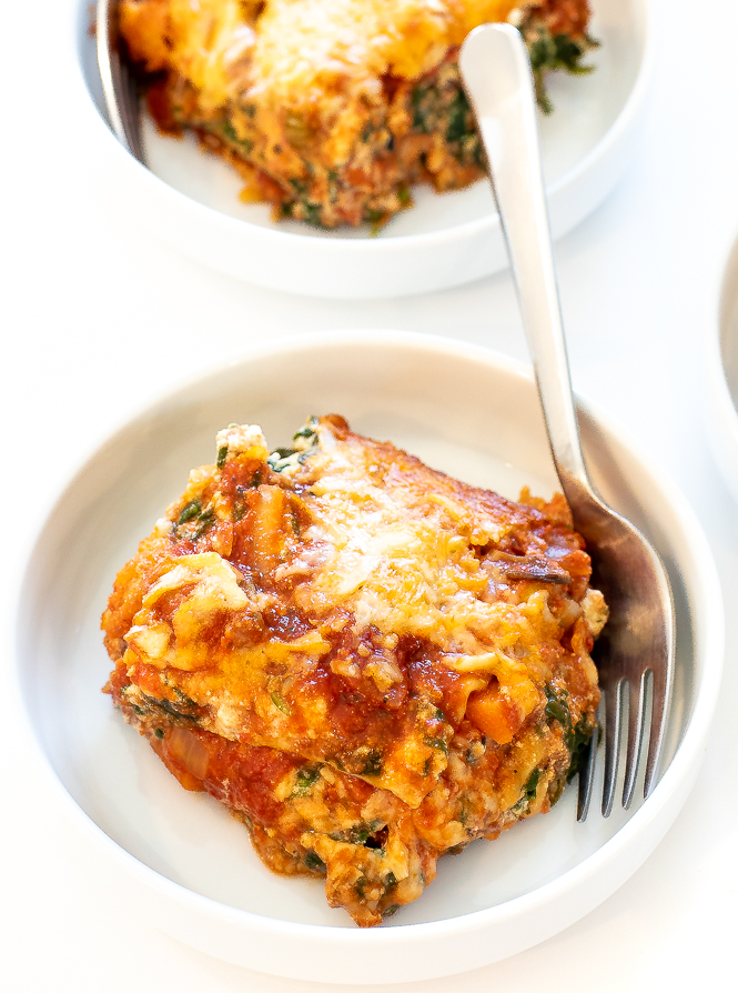 A slice of vegetarian lasagna on a white plate with a fork.