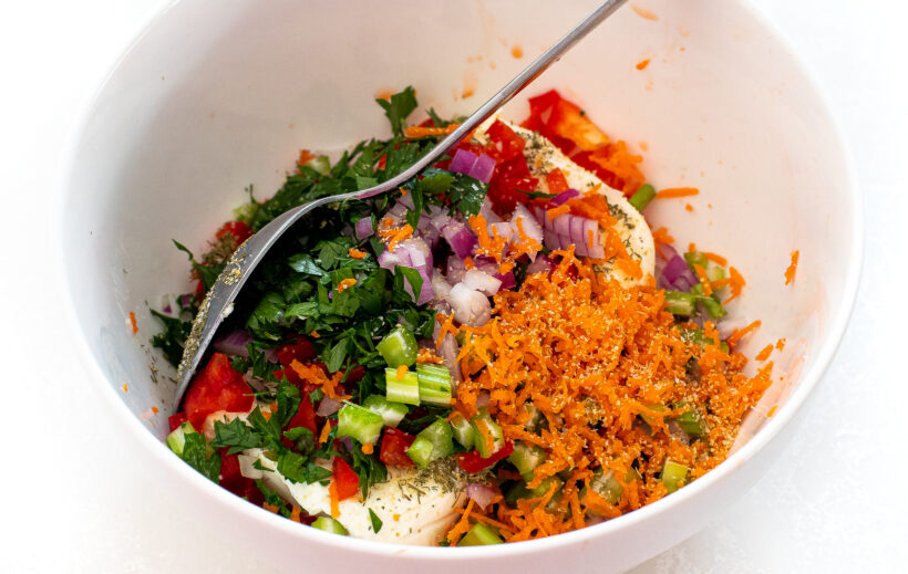 Ingredients for veggie cream cheese in a mixing bowl with a spoon.