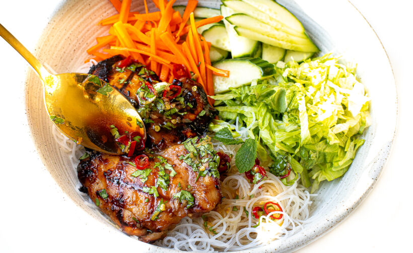 spooning sauce on top of vermicelli noodle bowls with thai chicken