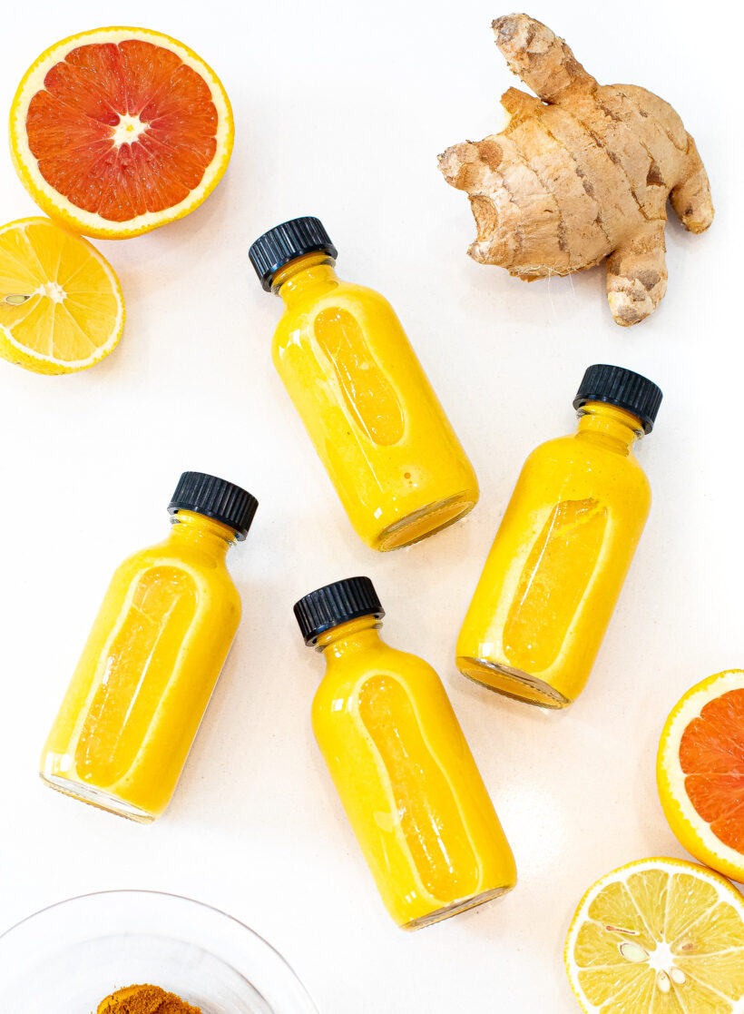 Overhead shot of wellness glow shots laid on a counter with citrus and ginger around them. 