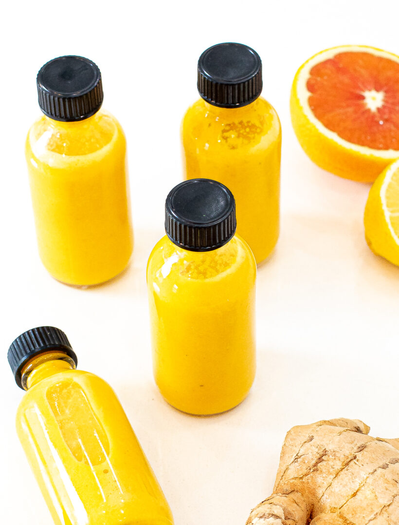 Small bottles filled with wellness shot drinks surrounded by citrus and ginger. 