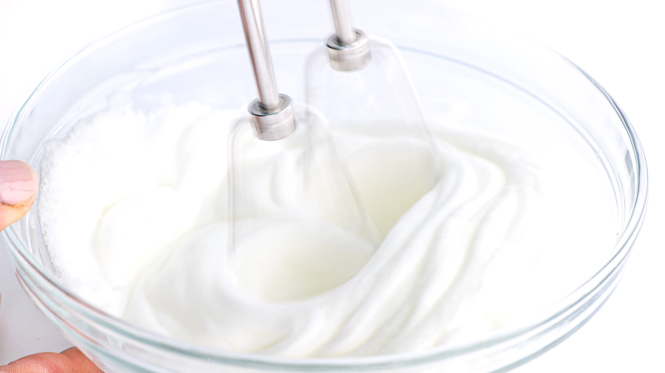 whipping egg whites in clear bowl with a hand held mixer
