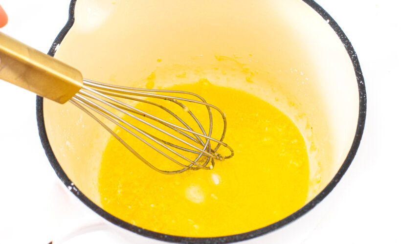 Cheese sauce in a saucepan with a whisk stirring it.