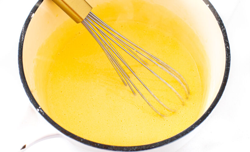 Cheese sauce in a sauce pan with a whisk stirring it.