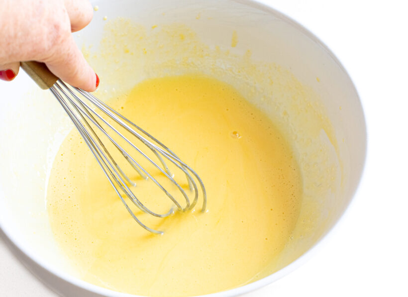 Hand whisking egg yolks and sugar together in a mixing bowl. 