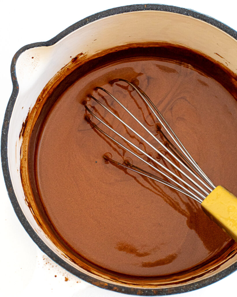 Chocolate syrup in a sauce pan with a whisk. 