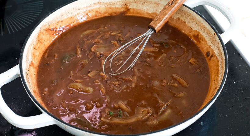 Onion gravy in a skillet with a whisk.