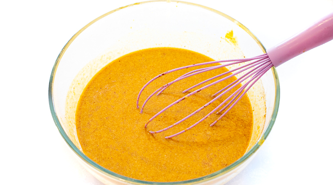 Wet ingredients in a glass bowl with a pink whisk.