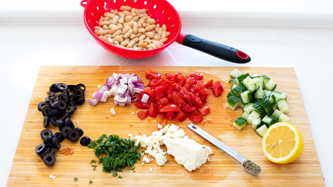 Ingredients needed for white bean salad laid out on a wooden cutting board.