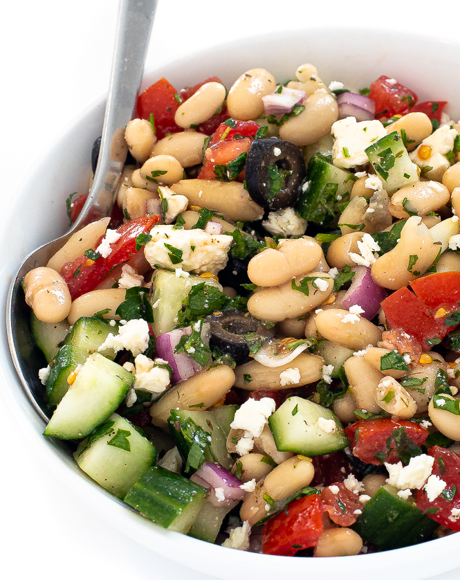White bean salad in a white bowl with a silver serving spoon.