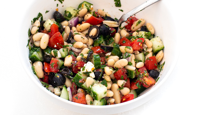 Salad after being mixed in a white bowl with a silver spoon.