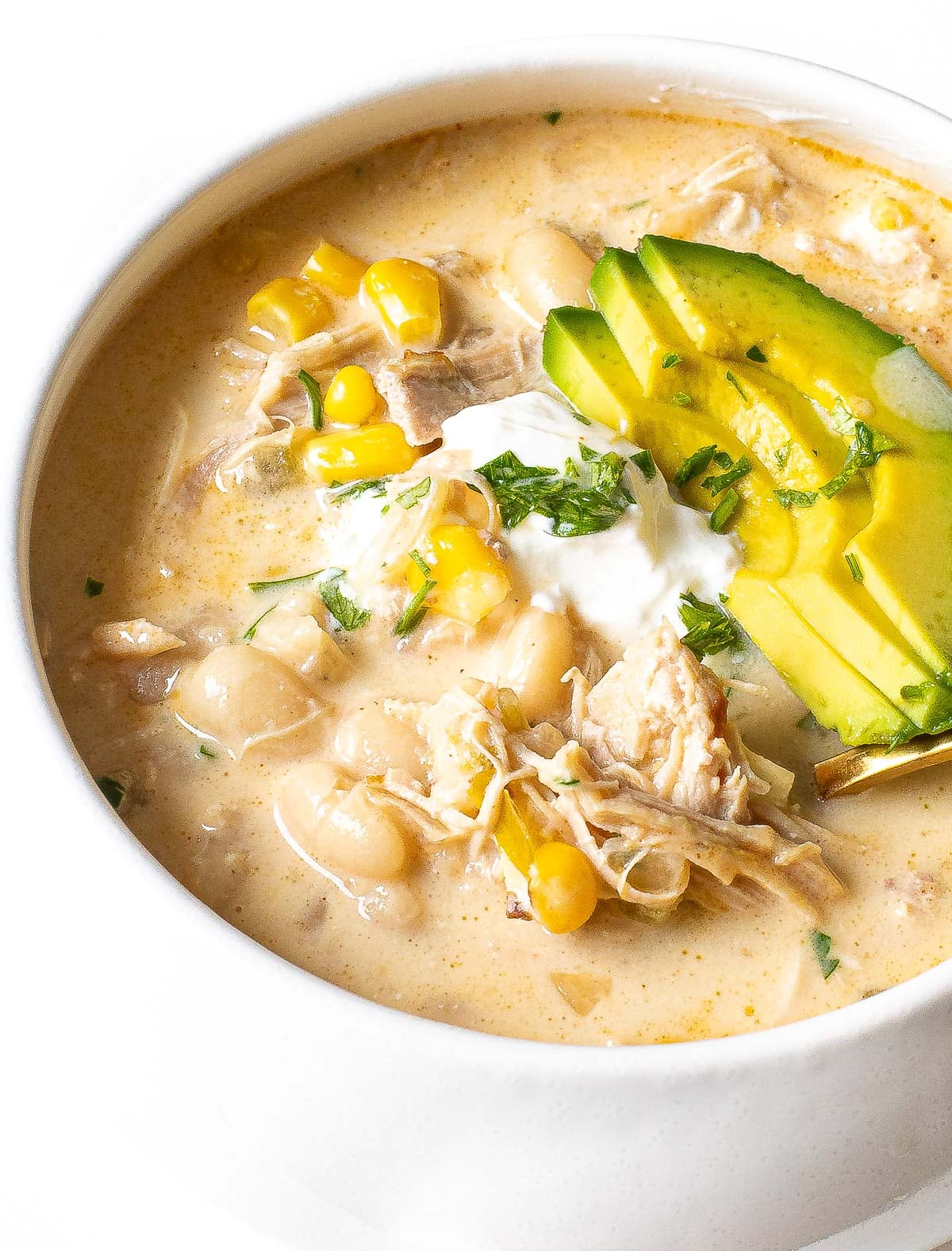 white chicken chili recipe in bowl topped with avocado, sour cream, corn and cilantro