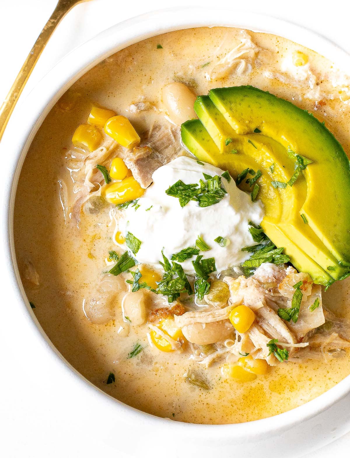 white chicken chili in bowl topped with avocado, sour cream and cilantro