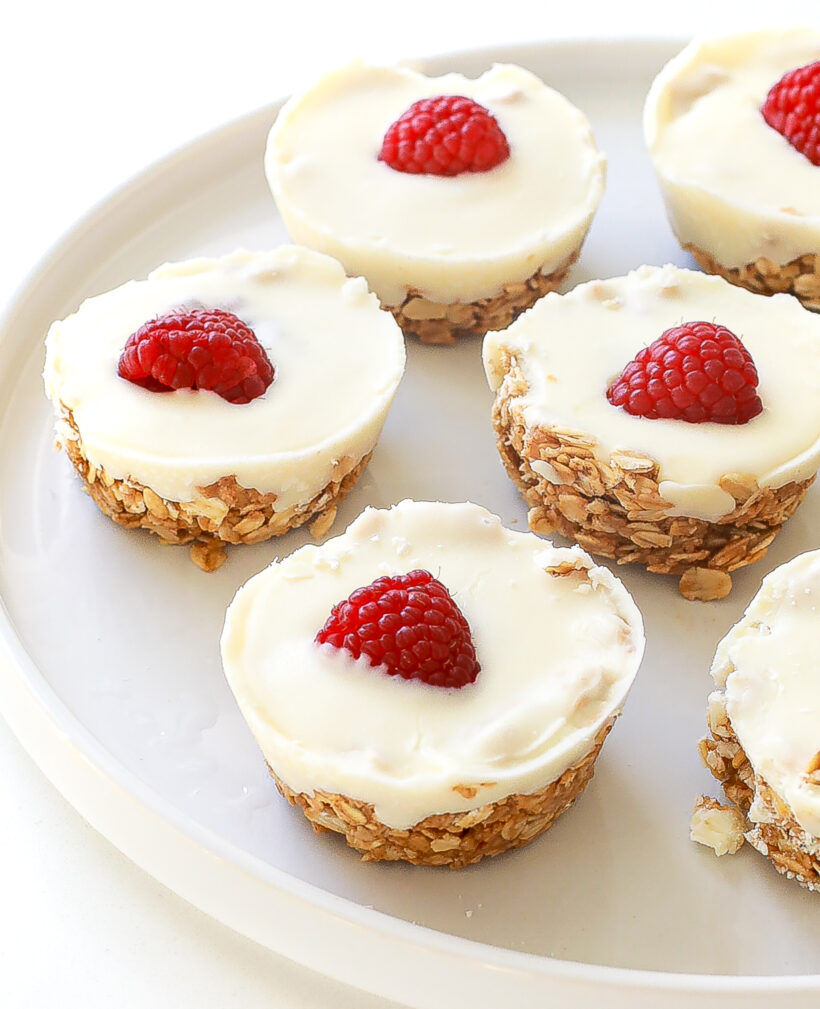 White chocolate oat cups served on a white plate with raspberries on top.
