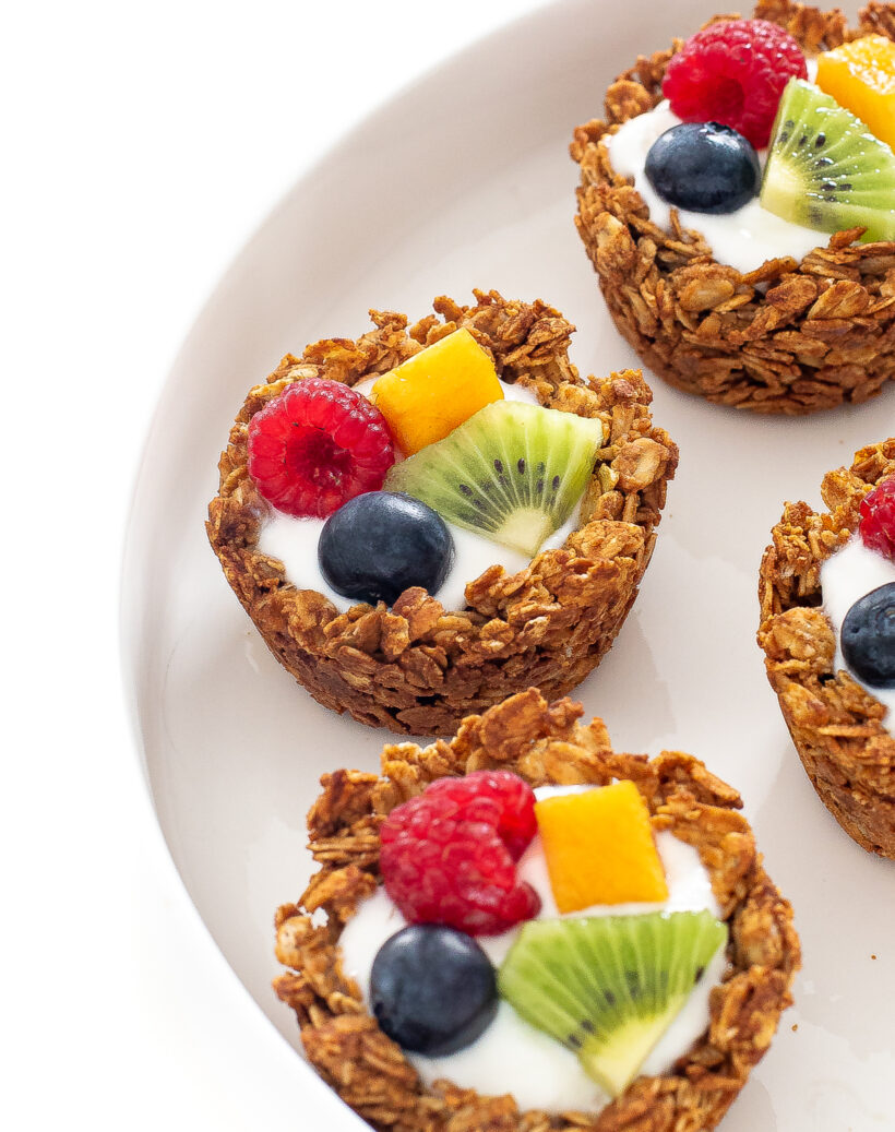 Granola cups with yogurt and fruit on them lined up on a white plate.