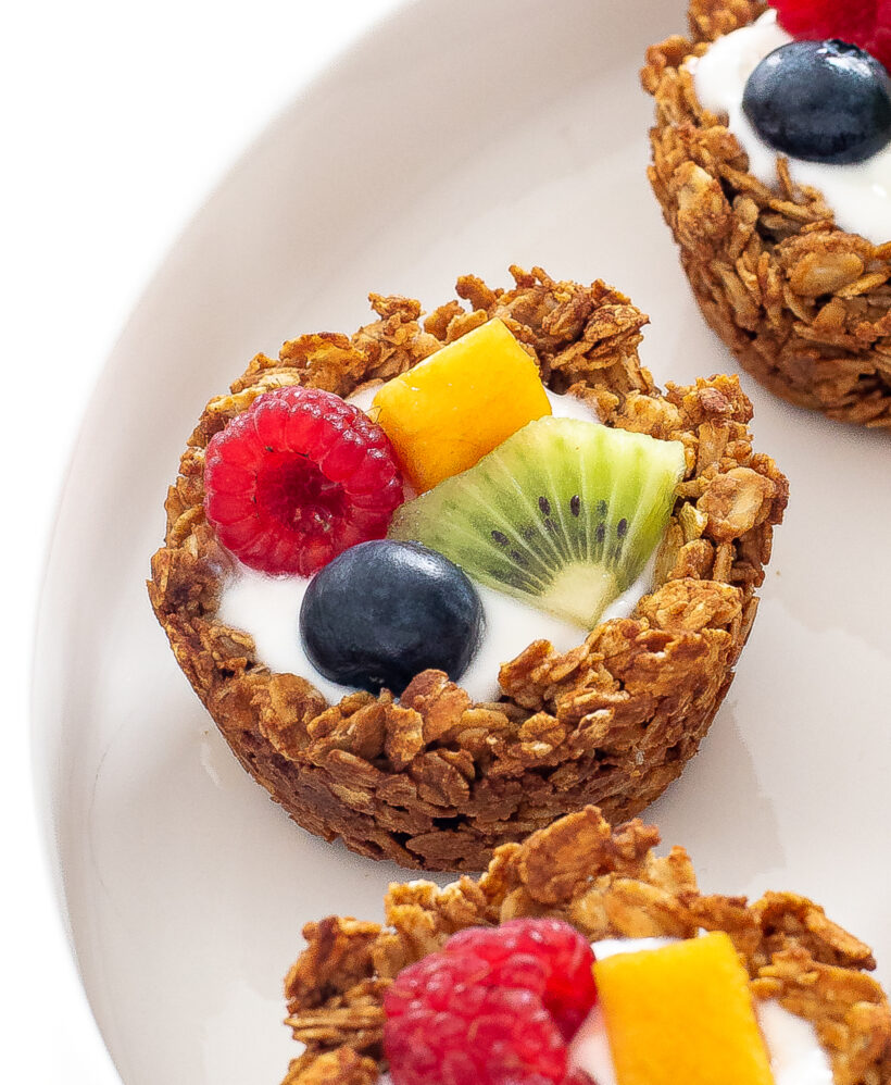 Granola cup with yogurt and fruit on top on a white plate.