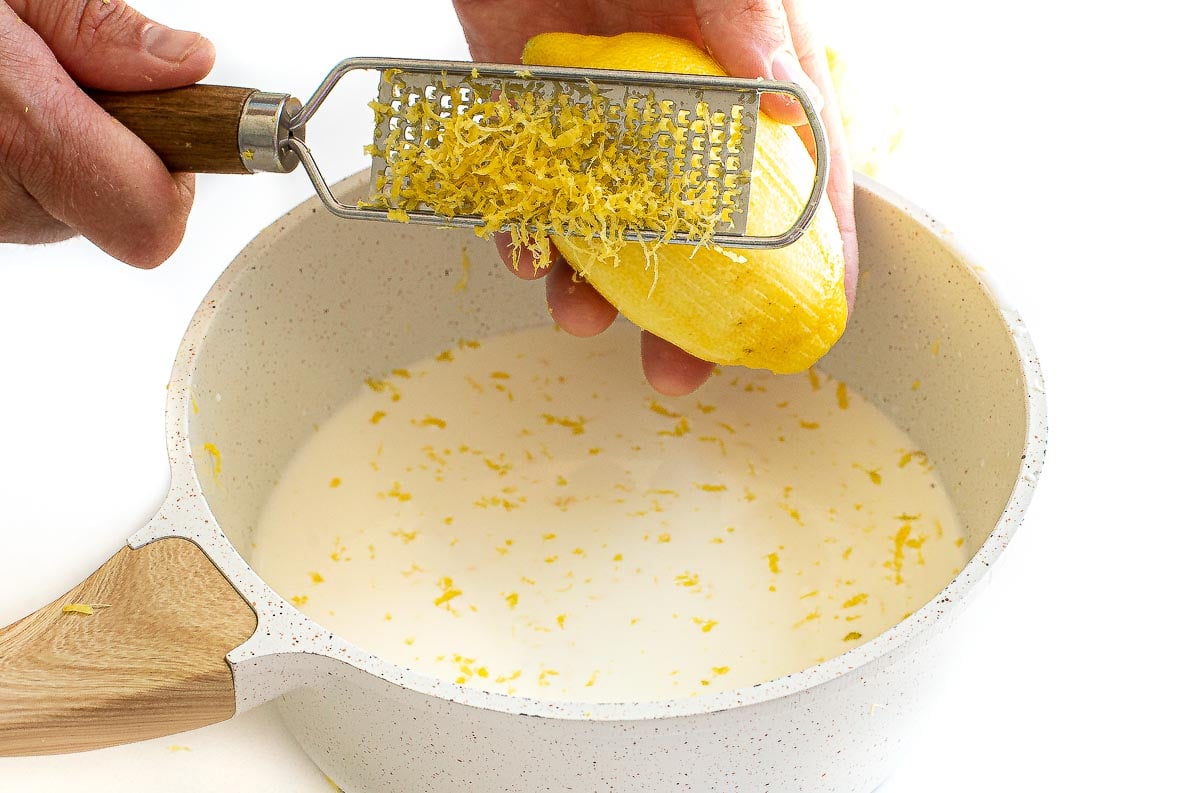 zesting lemon into cream and milk mixture in saucepan 