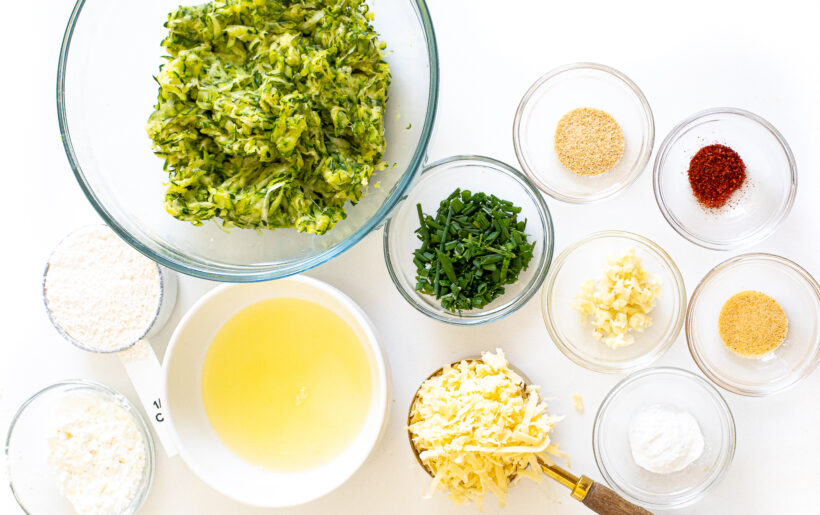 Ingredients for zucchini fritters laid out on a white surface.