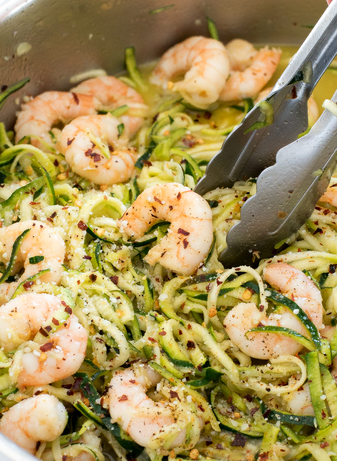 Silver tongs serving healthy shrimp scampi with zucchini noodles from a stainless steel pan.